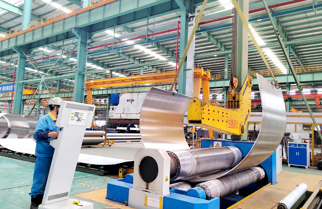 Large stainless steel coil being formed on a roll bending line during cylinder fabrication